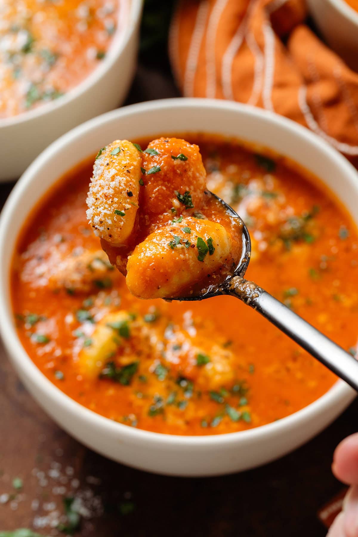 A spoon scooping three gnocchi from a bowl of tomato soup sprinkled with fresh herbs.