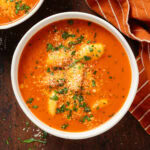 Creamy tomato gnocchi soup in a white bowl garnished with fresh herbs and parmesan.