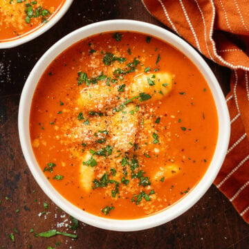 Creamy tomato gnocchi soup in a white bowl garnished with fresh herbs and parmesan.