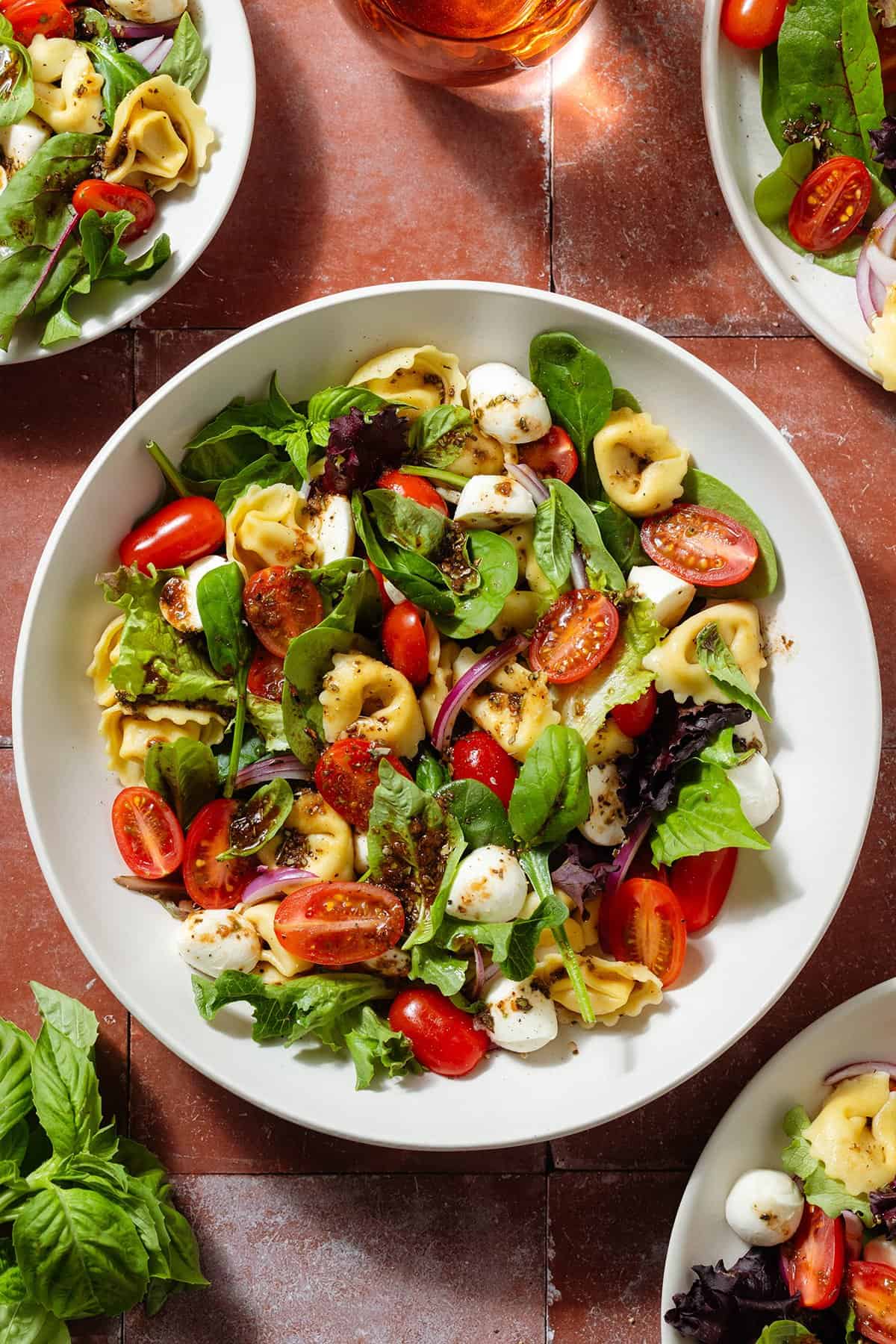 Tortellini caprese salad with mixed greens in a white bowl and more smaller plates around it.