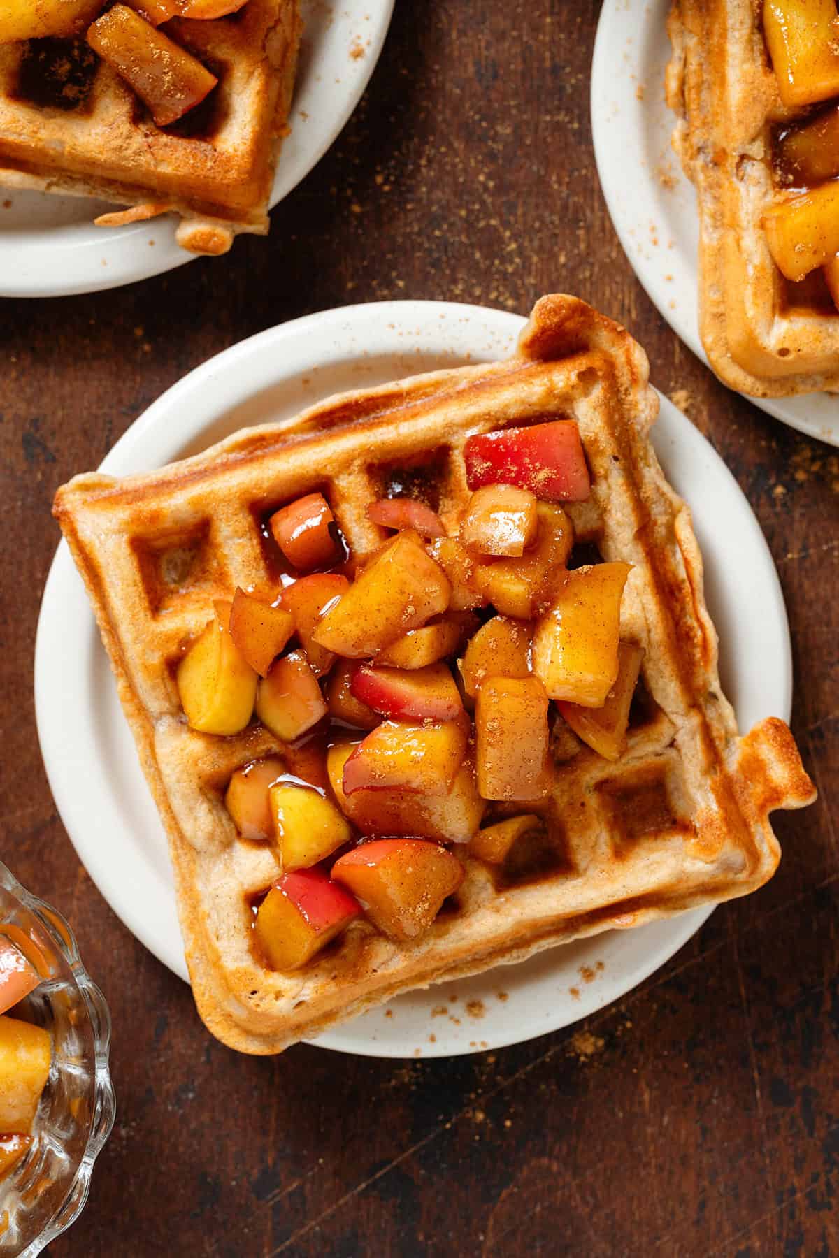 Small plates each with a single waffle topped with caramelized diced apples dusted with cinnamon.