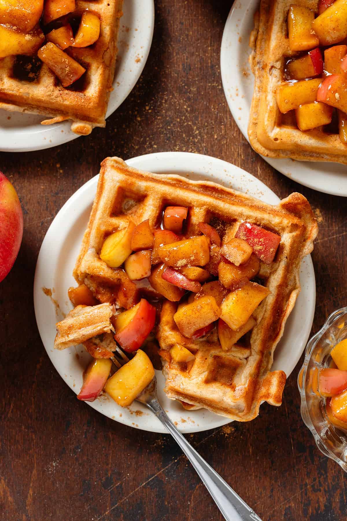 Small plates each with a single waffle topped with caramelized diced apples with a fork grabbing a corner bite from the middle plate.