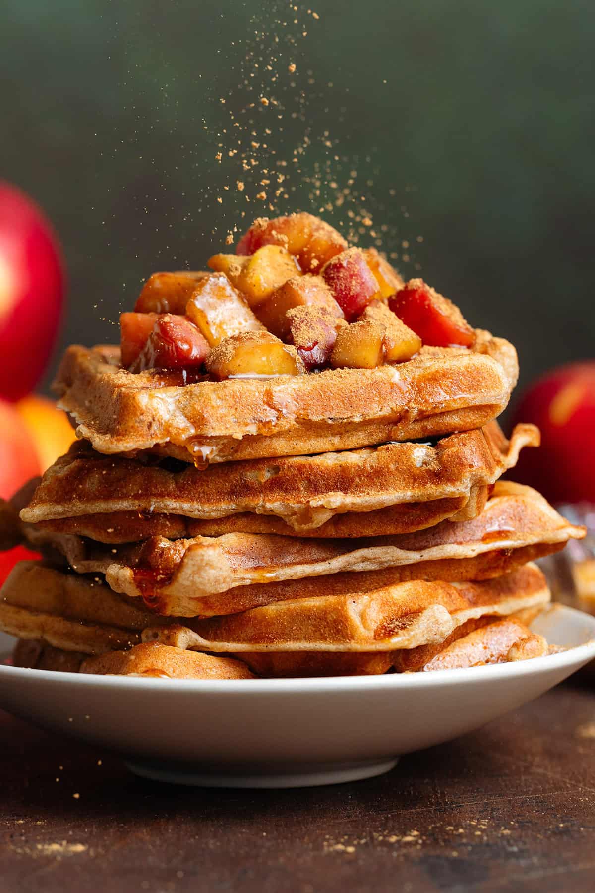 A stack of waffles with caramelized apples on top being dusted with cinnamon.