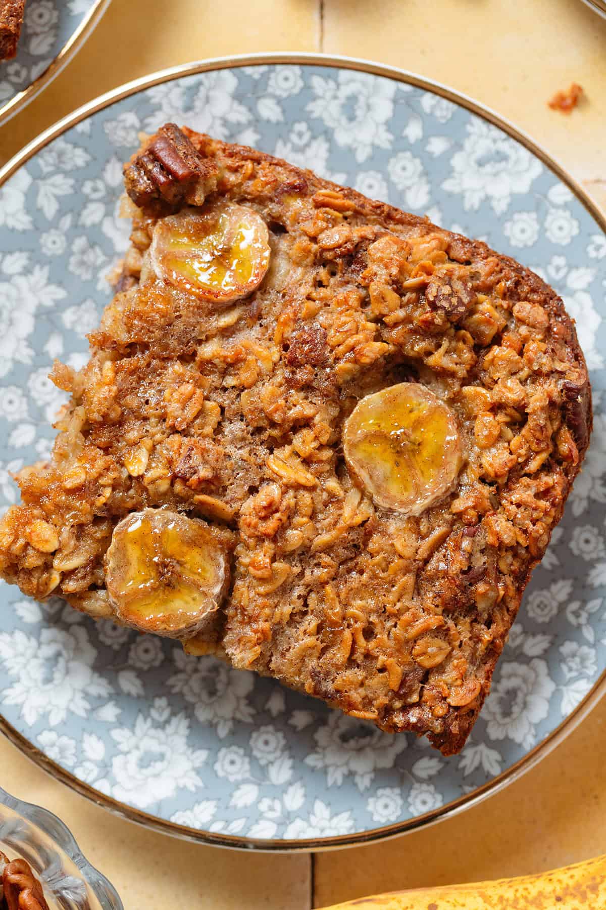 A slice of banana baked oatmeal with caramelized banana slices baked into it on top on a blue floral plate.