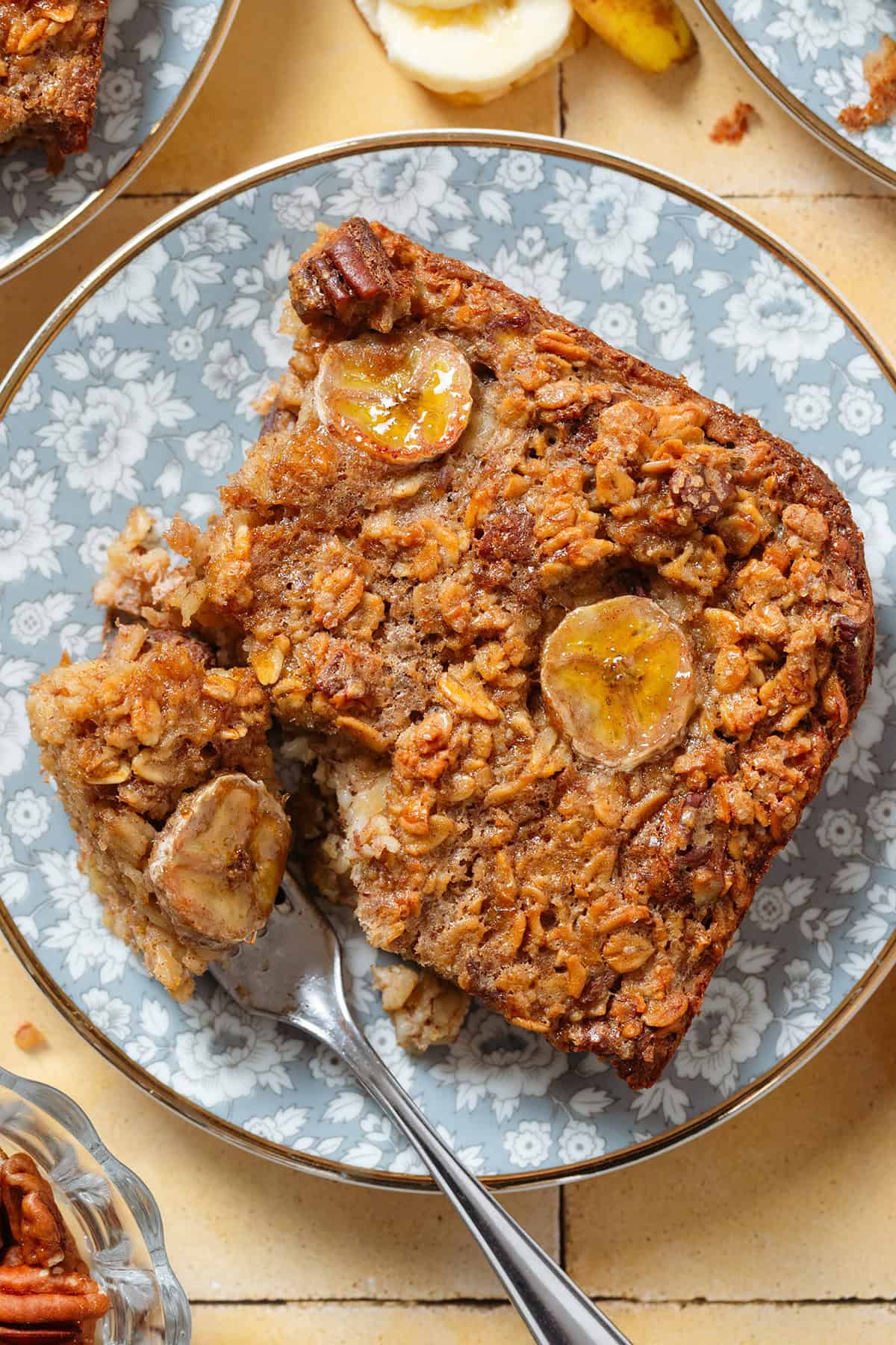 A banana baked oatmeal square caramelized on top on blue floral plate with a fork slicing into one corner.