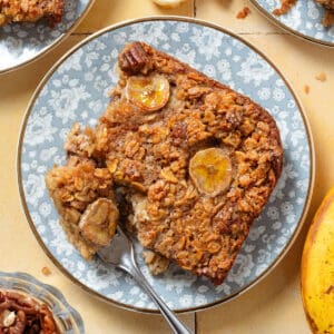 A slice of banana baked oatmeal with caramelized banana slices baked into it on top on a blue floral plate.