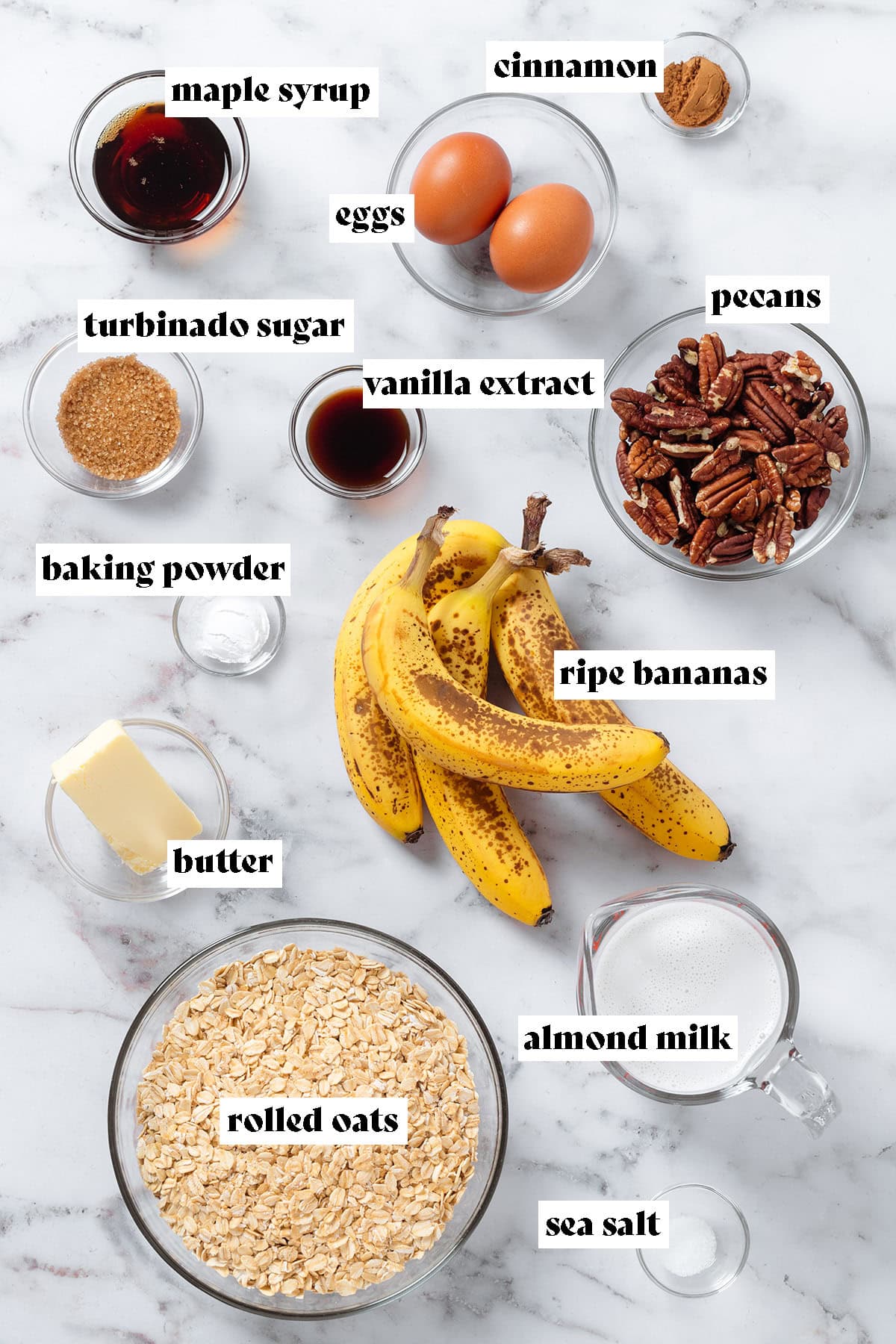 Ripe bananas, oats, pecans, eggs, spices, butter, and other measured ingredients in small glass bowls with text overlay.