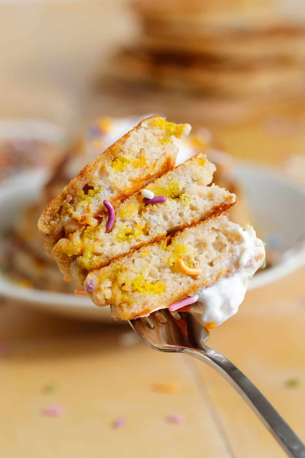 A fork holding a bite-sized piece of a stack of pancakes showing the fluffy inside with sprinkles.