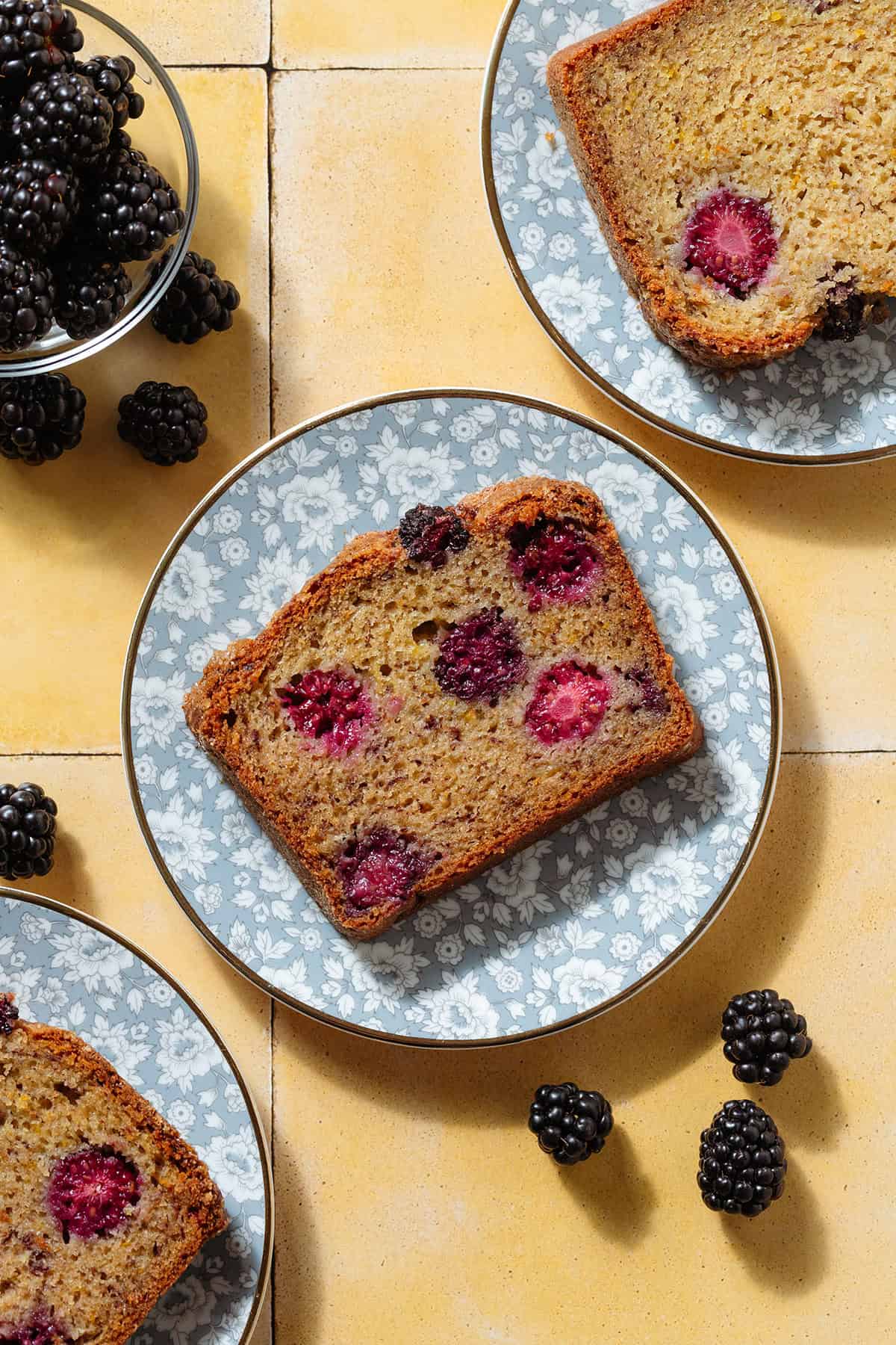 Slices of blackberry banana bread showing multiple blackberries inside on blue floral plates.
