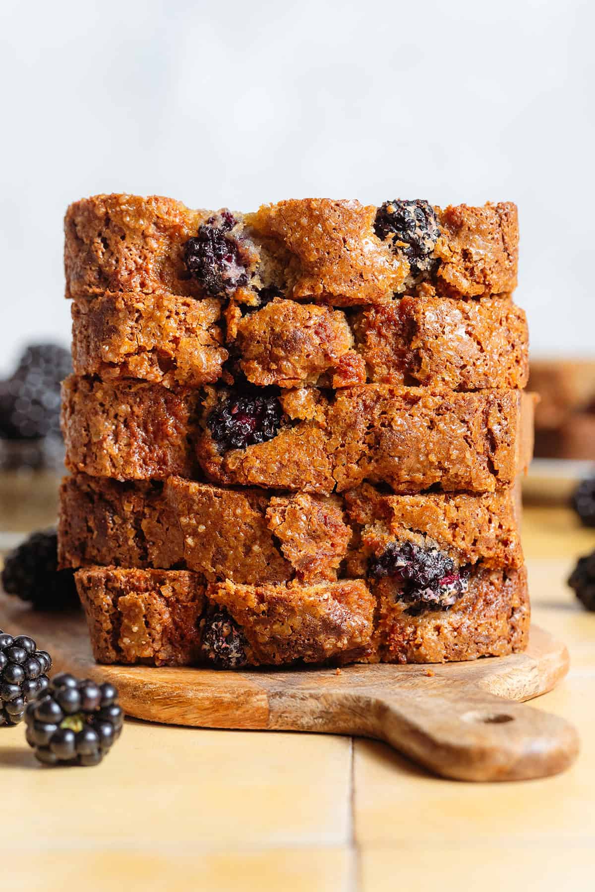 A stack of banana bread with whole blackberries inside on a small wooden cutting board.
