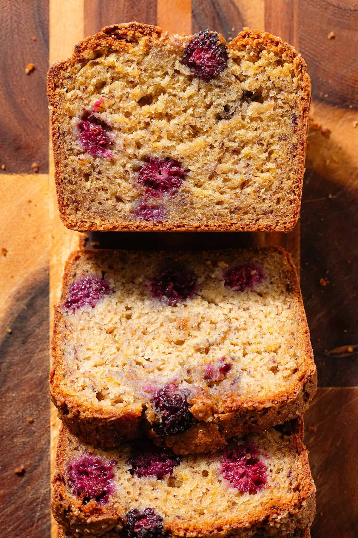 Slices of banana bread on a wooden cutting board showing the blackberries inside.