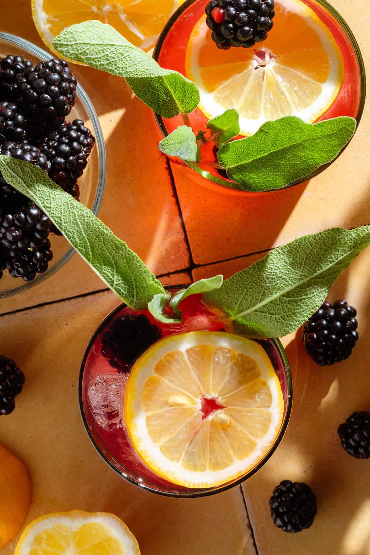 Blackberry lemonade in short glasses garnished with fresh blackberries, sage, and lemon.