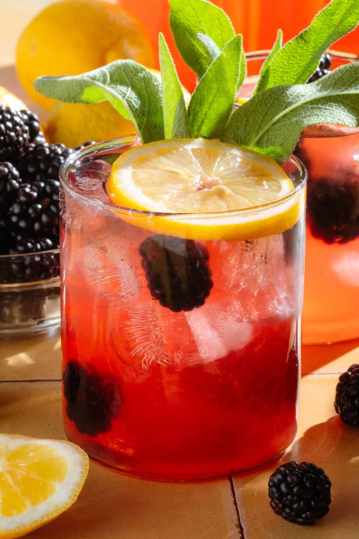 Dark red lemonade in a short glass garnished with blackberries, a lemon slice, and fresh thyme.