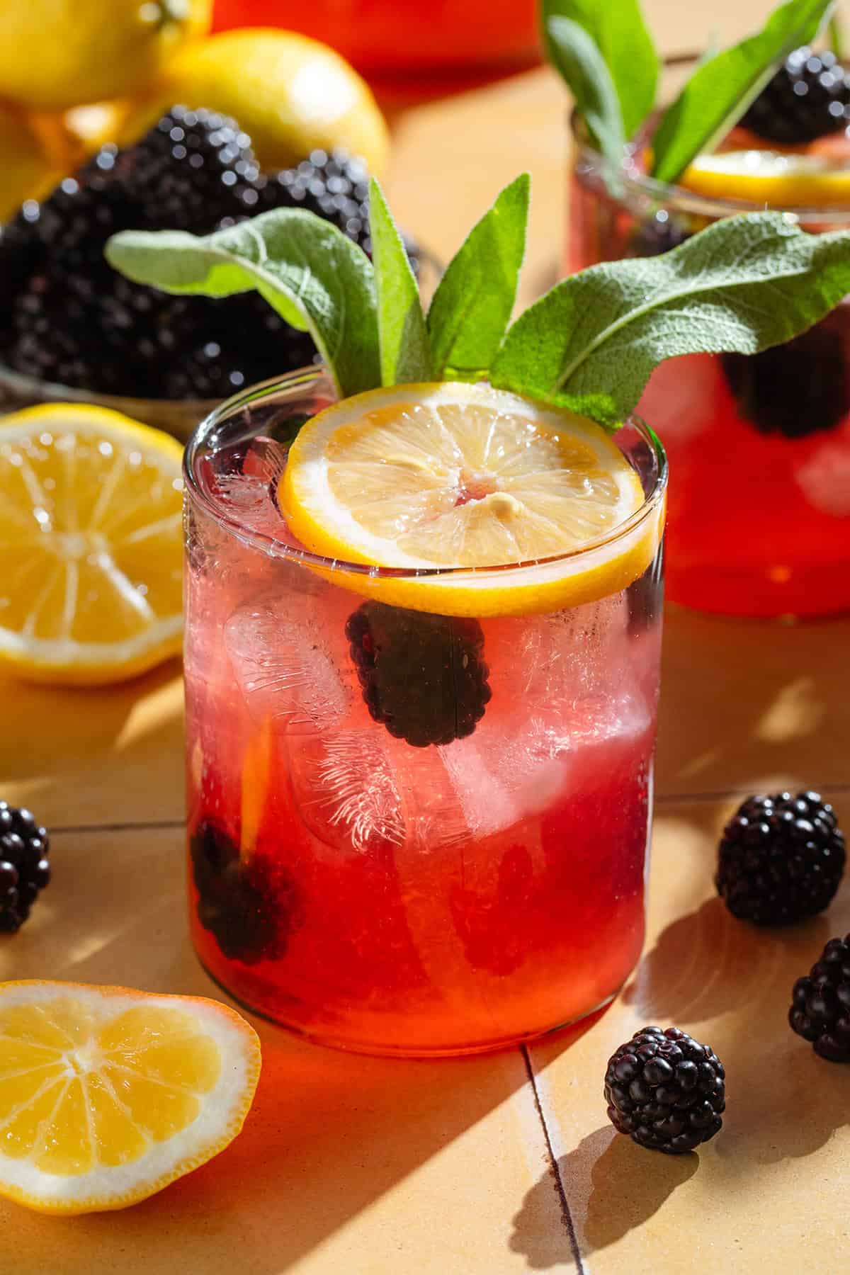 Dark red lemonade in a short glass garnished with blackberries, a lemon slice, and fresh thyme.
