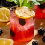 Dark red lemonade in a short glass garnished with blackberries, a lemon slice, and fresh thyme.
