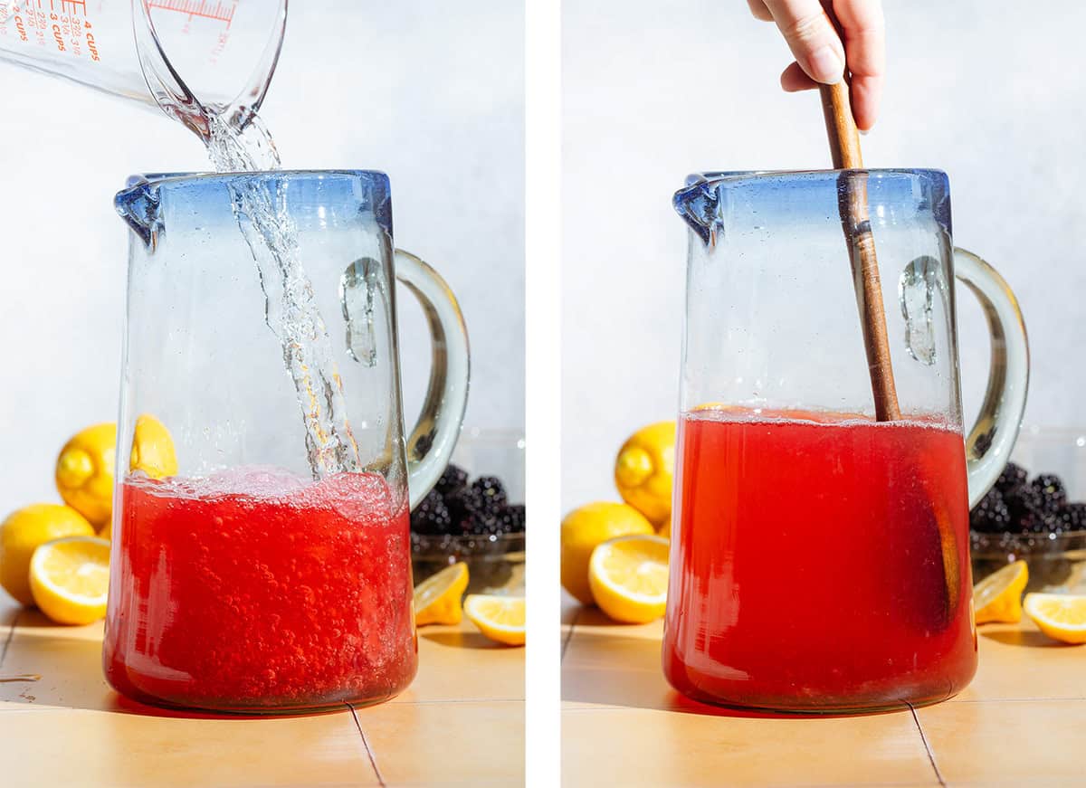 Water being poured into a large pitcher with blackberry syrup and lemon juice and stirred.