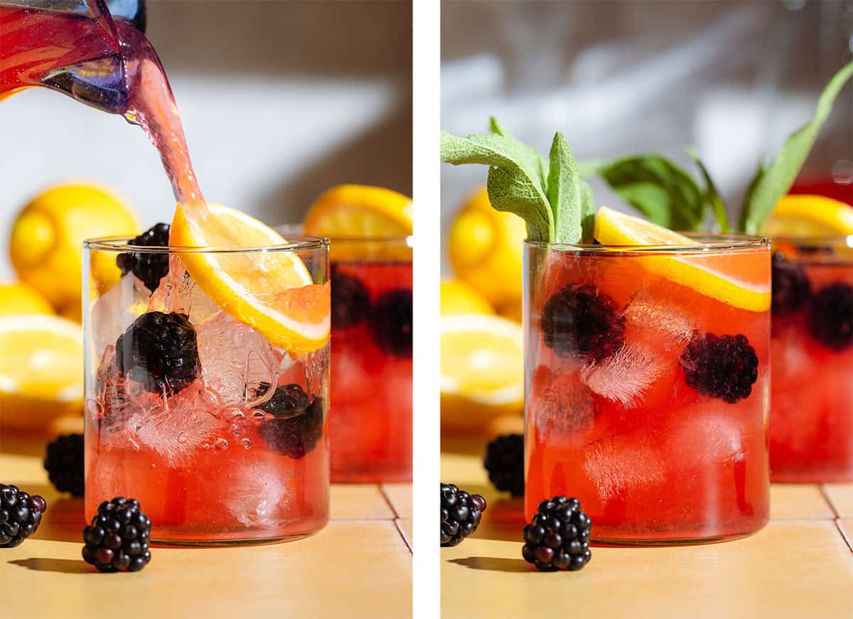 Dark red lemonade being poured into a short glass over ice garnished with a lemon slice and fresh sage.