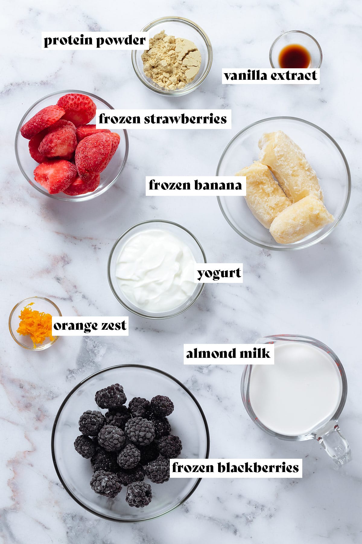 Ingredients like frozen blackberries, bananas, strawberries, almond milk, and yogurt in small glass bowls with text overlay.