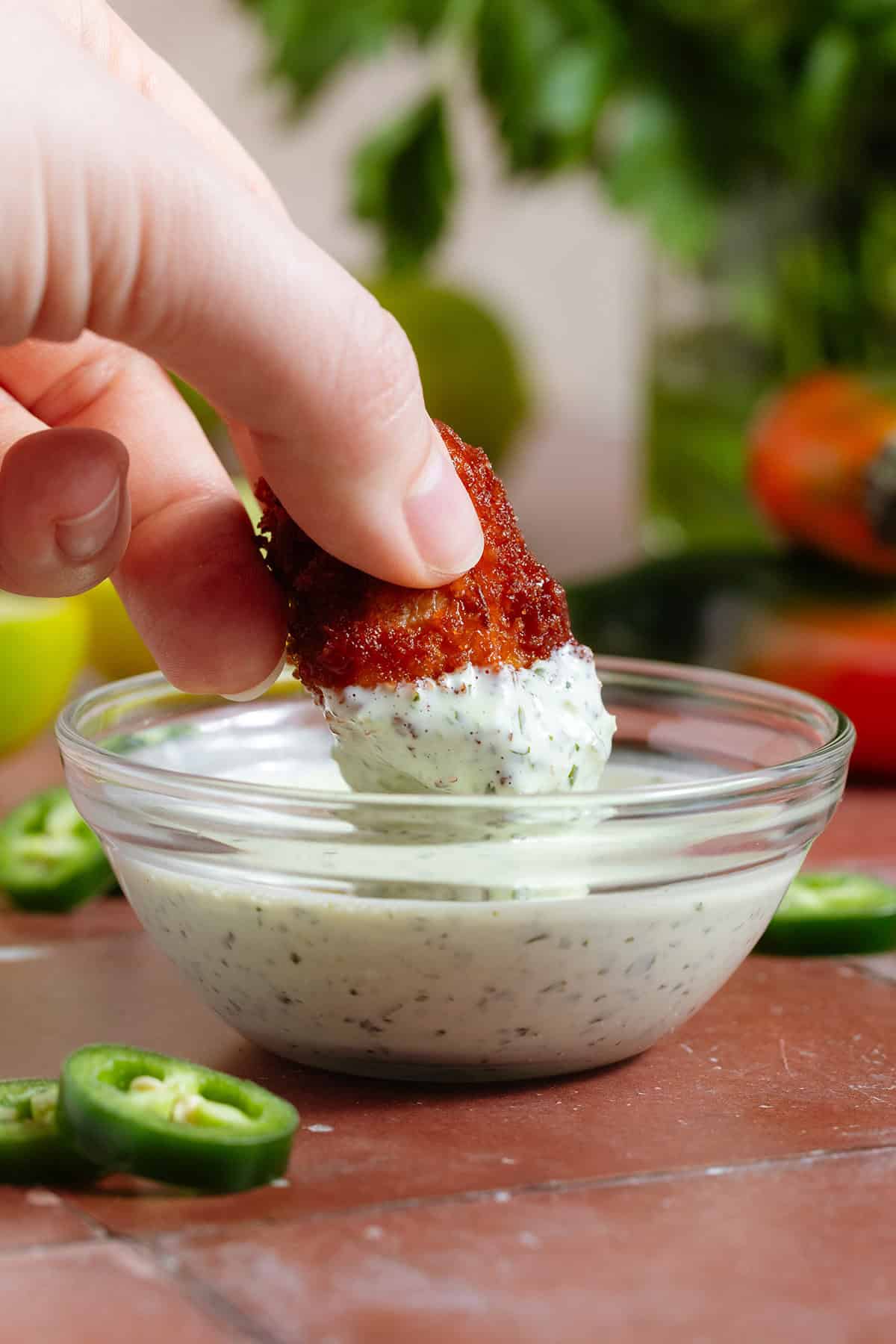 A hand dipping a cauliflower wing into creamy jalapeno mayo with visible tiny pieces of jalapenos.