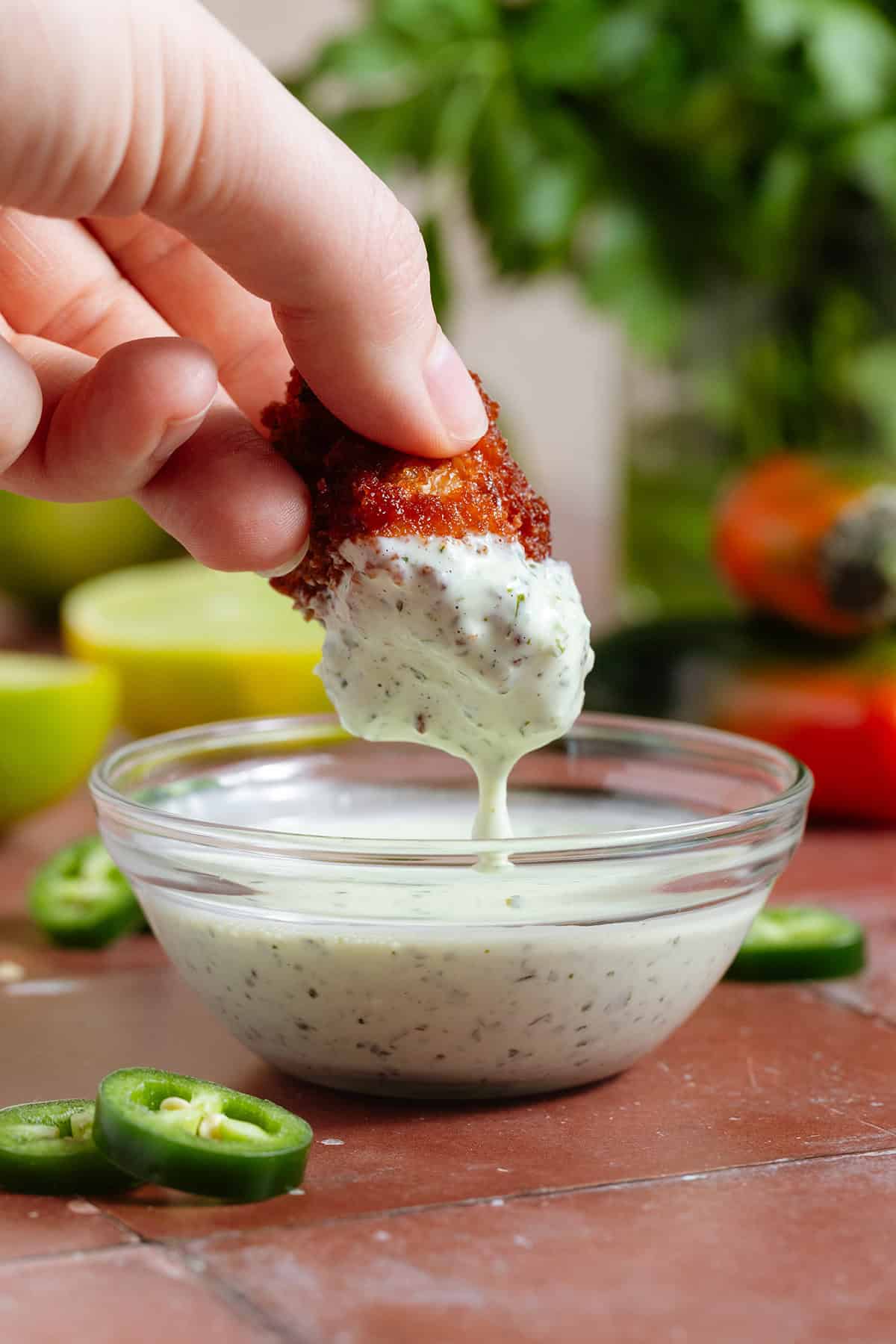 A hand dipping a cauliflower wing into creamy jalapeno mayo with visible tiny pieces of jalapenos.