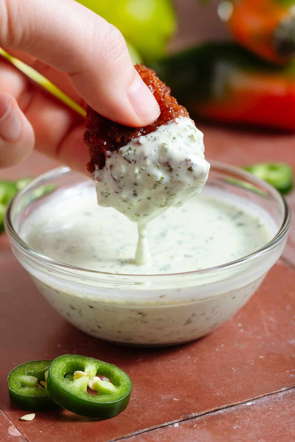 A hand dipping a cauliflower wing into creamy jalapeno mayo with visible tiny pieces of jalapenos.