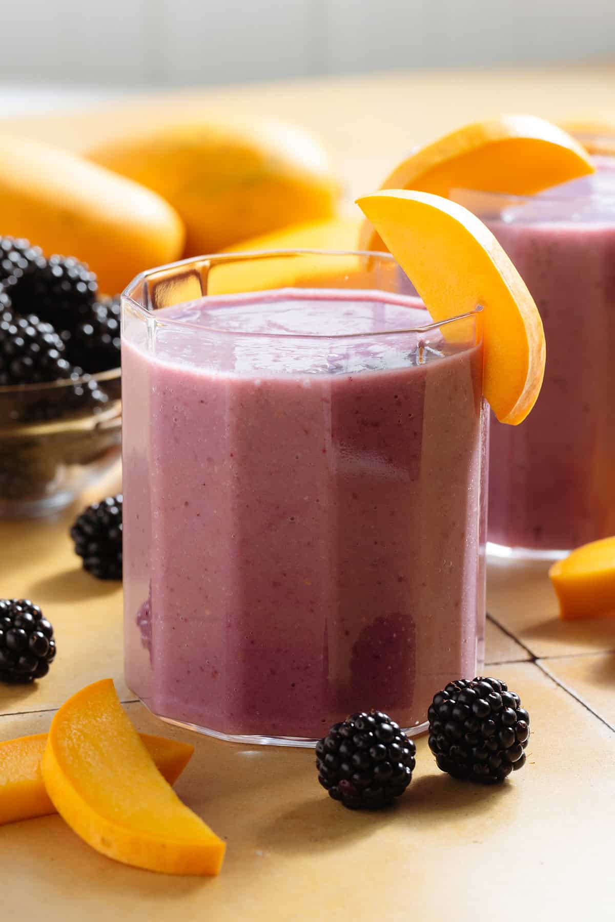 Vibrant purple smoothie in a short glass garnished with blackberries and slices of mango.