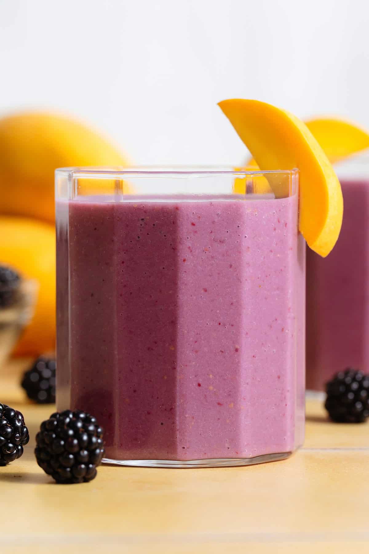 Vibrant purple smoothie in a short glass garnished with blackberries and slices of mango.