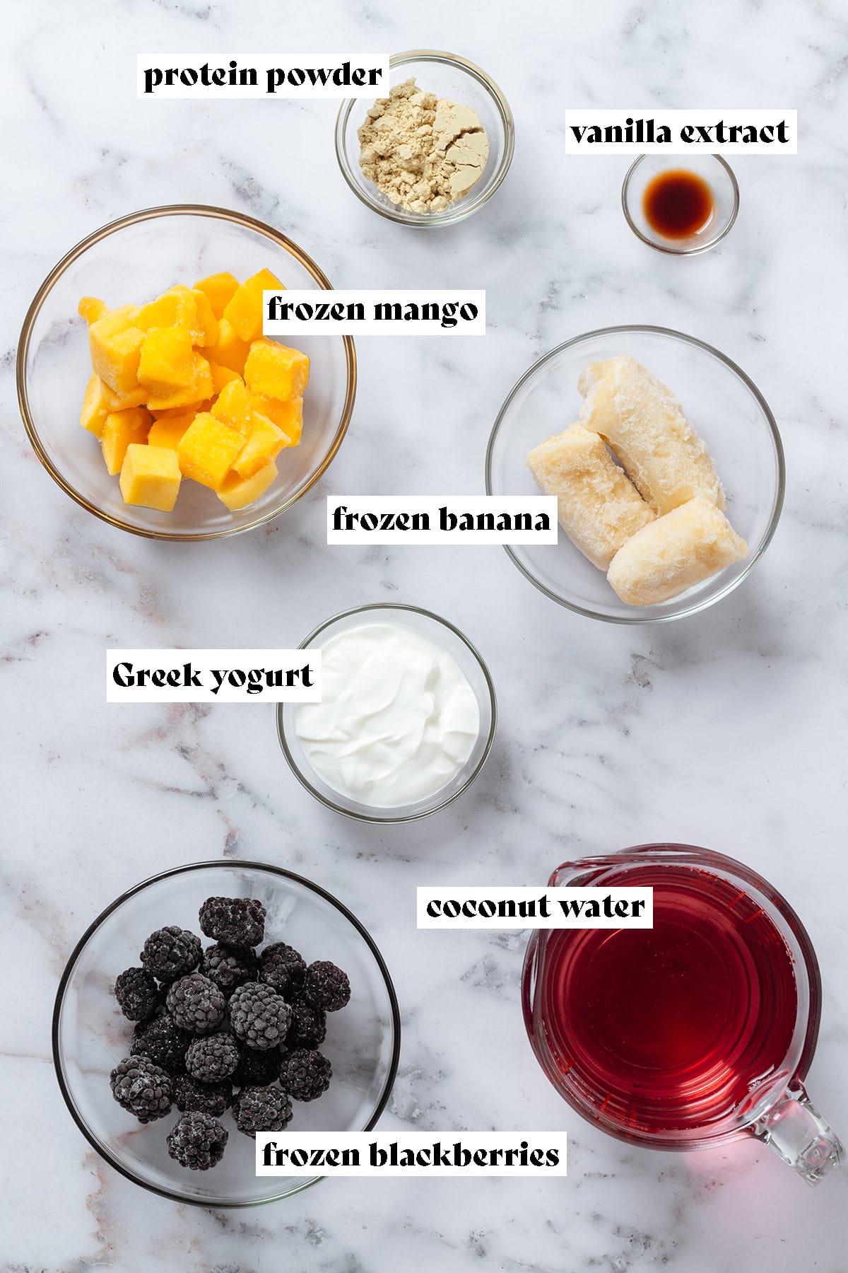 Small glass bowls with ingredients like frozen mango, banana, blackberries, coconut water, and Greek yogurt.