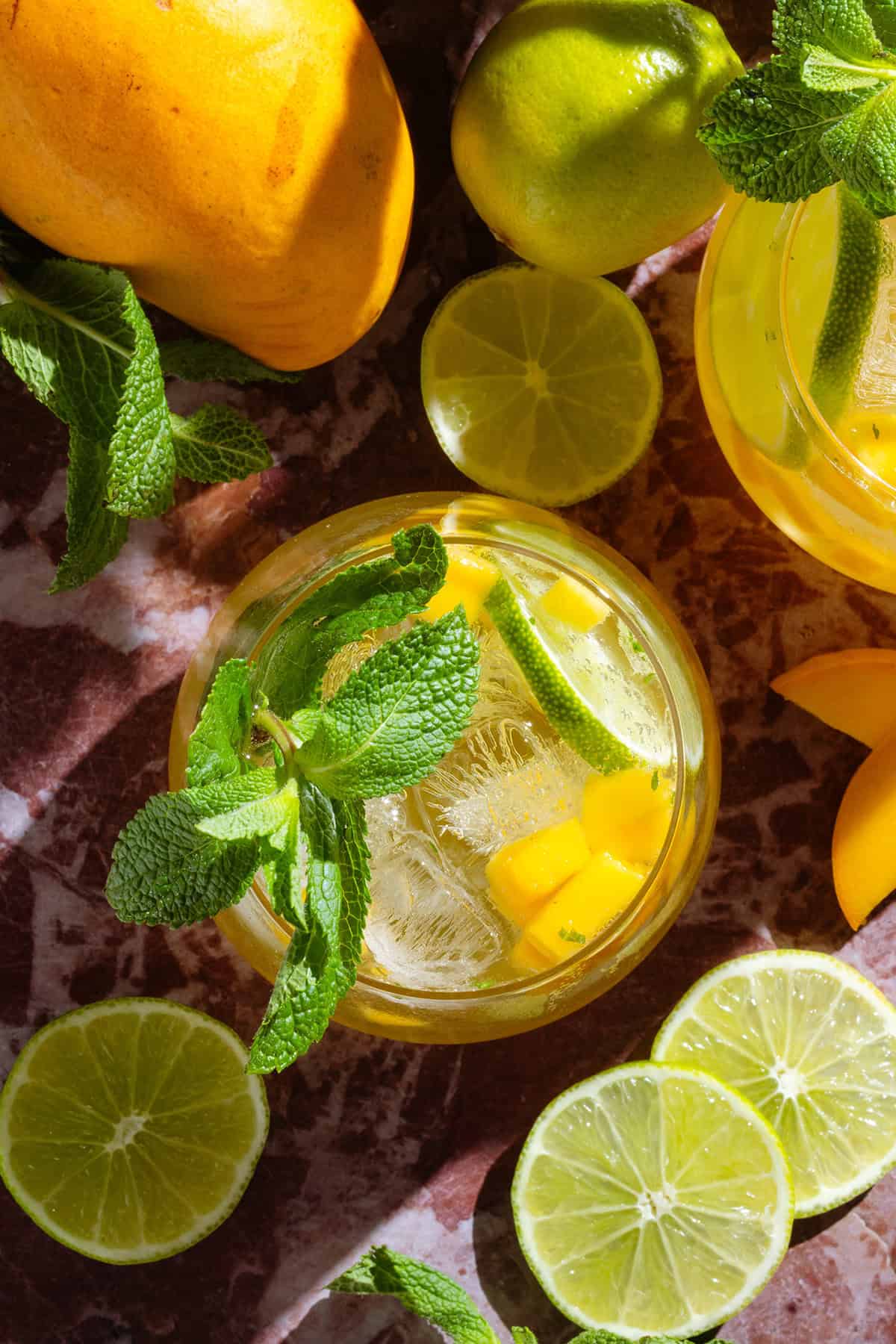 Bright yellow mango drink in a short glass garnished with fresh mint, a lime slice, and diced mango.