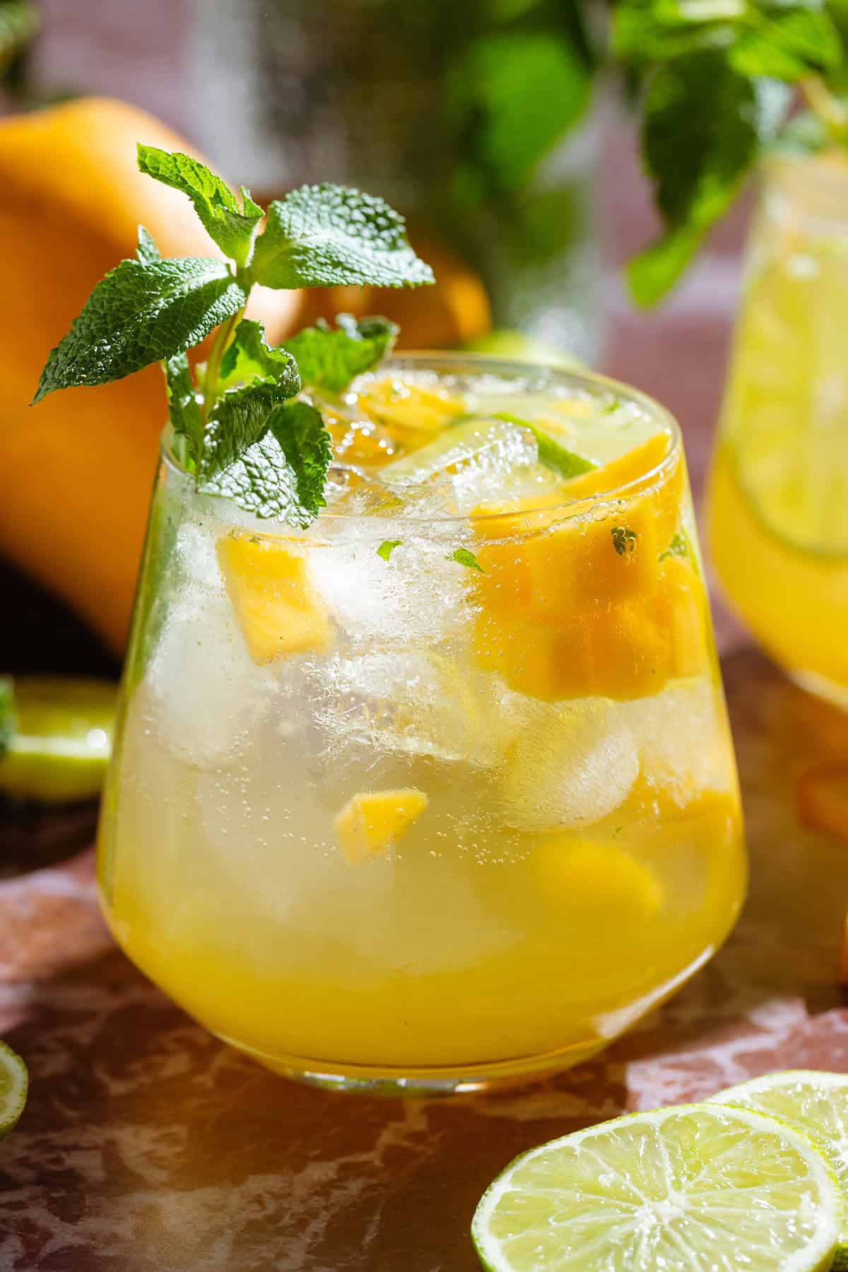 Bright yellow mango drink in a short glass garnished with fresh mint and diced mango.