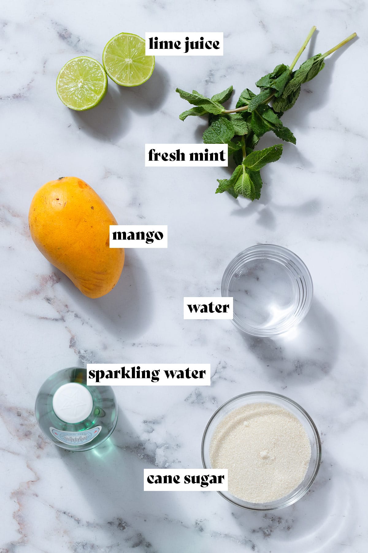 Mango, lime, fresh mint, sparkling water, and sugar on a marble background with text overlay.
