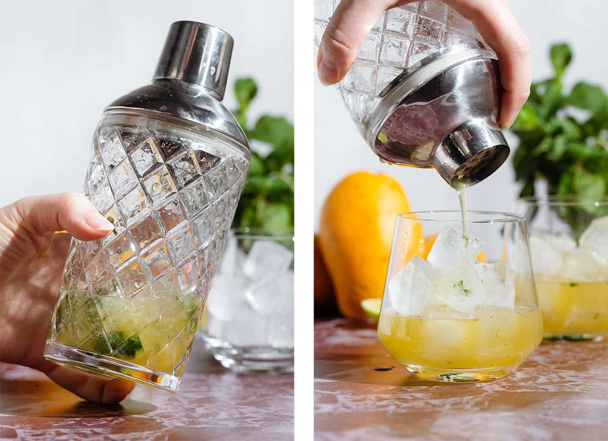 A glass cocktail shaker with mango drink being strained into a short glass over ice.
