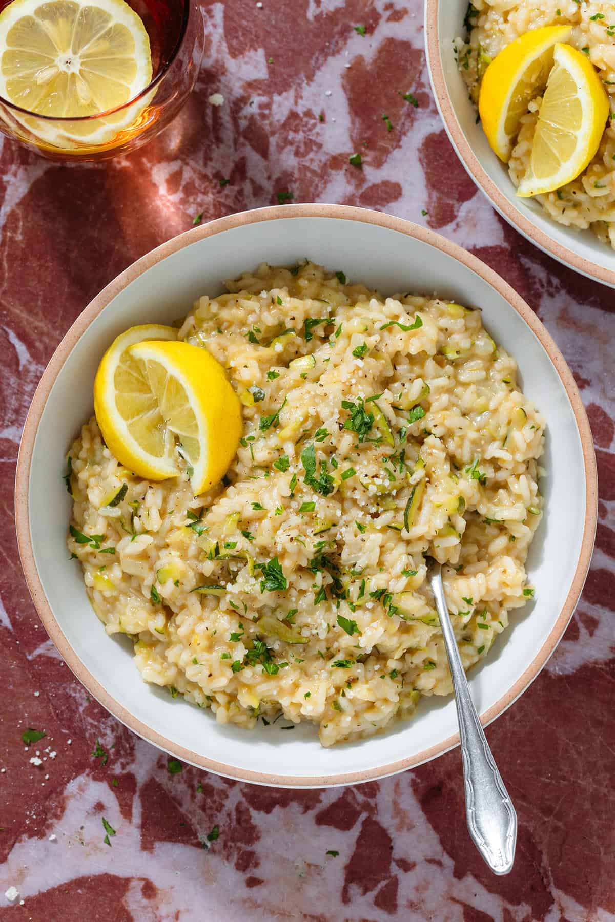 Creamy zucchini risotto garnished with fresh parsley and lemon wedges in a low bowl with a beige rim and with a fork.
