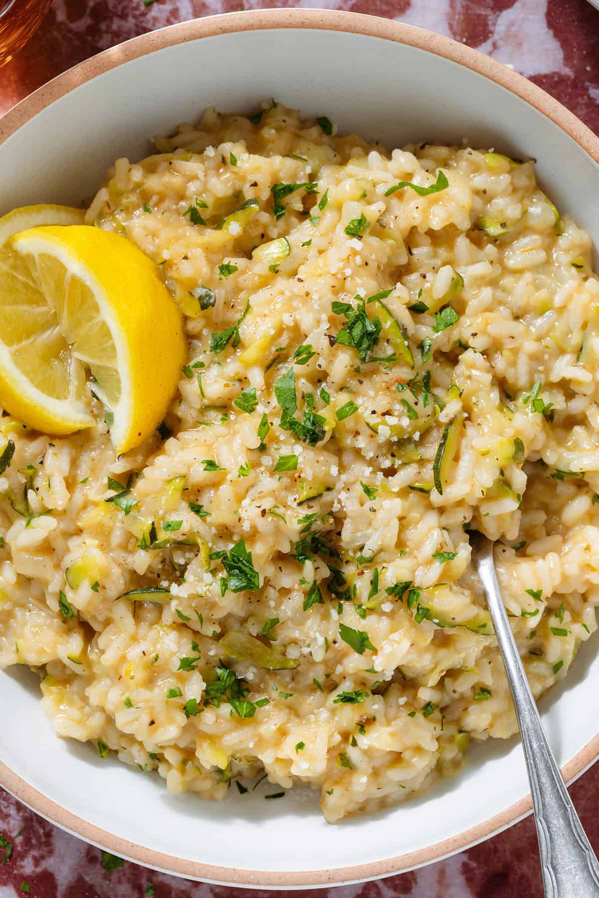 Creamy zucchini risotto garnished with fresh parsley and lemon wedges in a low bowl with a beige rim and with a fork.
