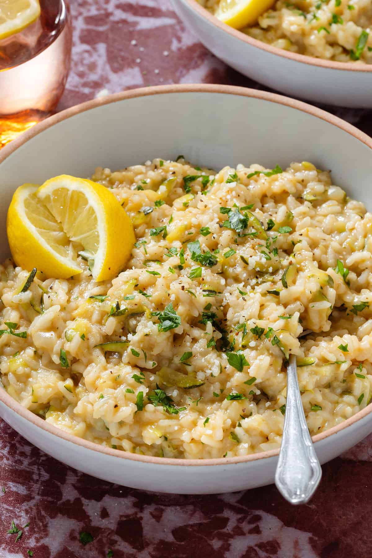 Creamy zucchini risotto garnished with fresh parsley and lemon wedges in a low bowl with a beige rim and with a fork.