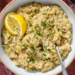 Creamy zucchini risotto garnished with fresh parsley and lemon wedges in a low bowl with a beige rim and with a fork.