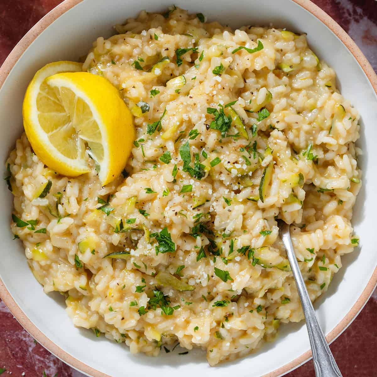 Creamy zucchini risotto garnished with fresh parsley and lemon wedges in a low bowl with a beige rim and with a fork.