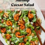 Caesar salad with spicy shrimp on a large oval serving platter with wooden serving spoons.