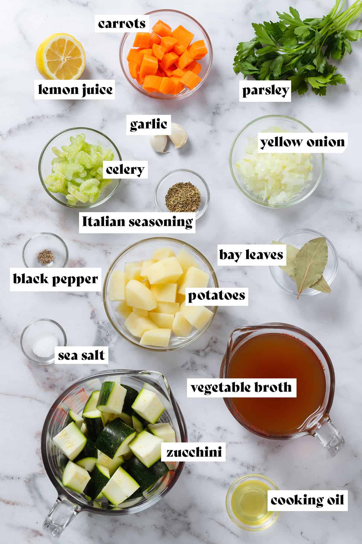 Small glass bowls with chopped celery, carrots, onion, potatoes, zucchini, spices, and other ingredients on a grey background.