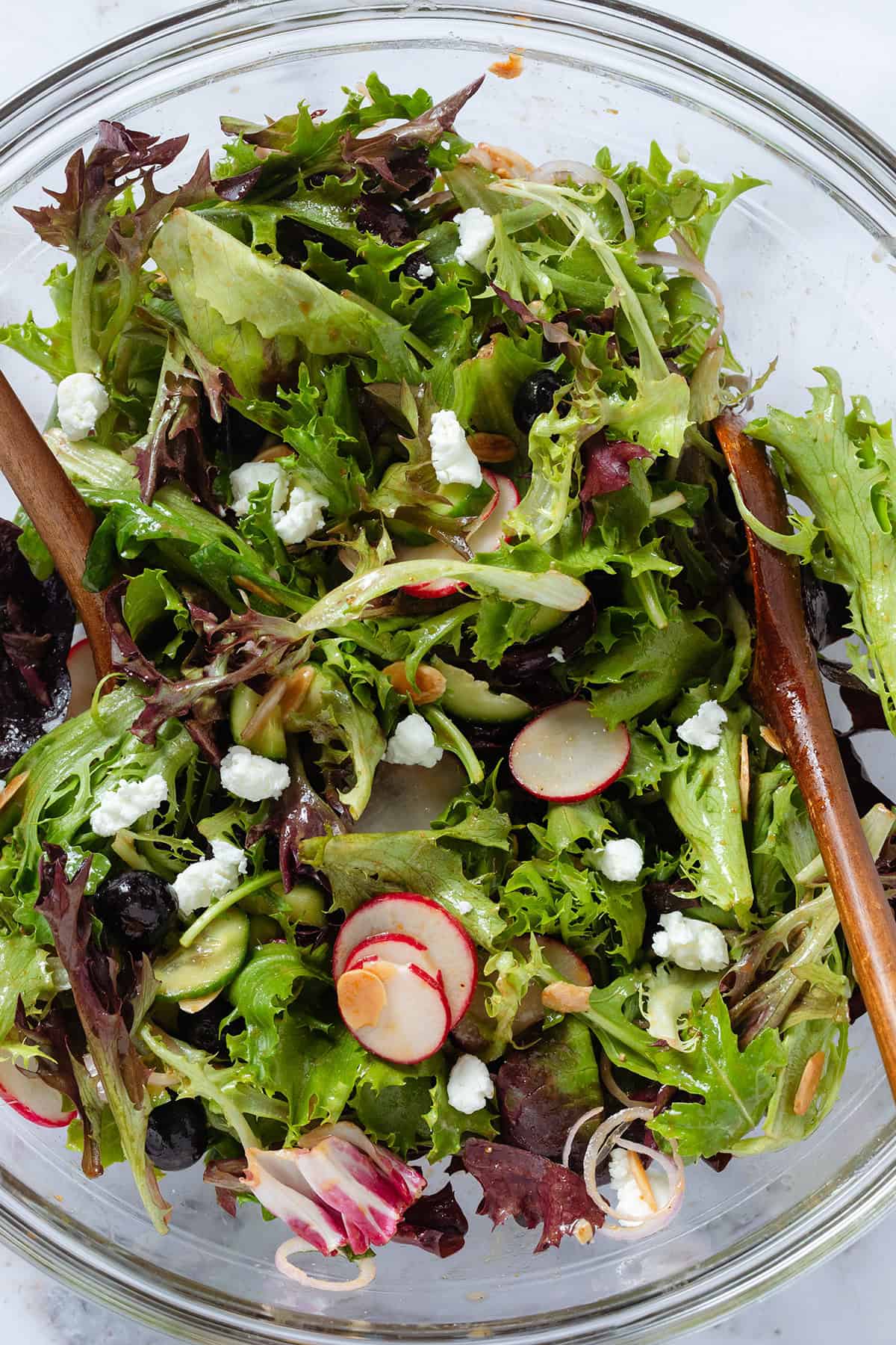 Blueberry salad with mixed greens, radishes, toasted almonds, shallots, and crumbled soft goat cheese in a large mixing bowl.