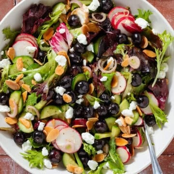 A bowl on blueberry salad with mixed greens, radishes, toasted almonds, and shallots.