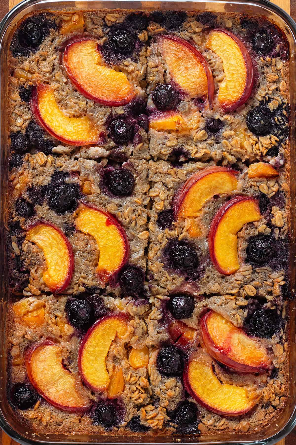Baked oatmeal with blueberries and peach slices in a glass baking dish sliced into 6 servings.