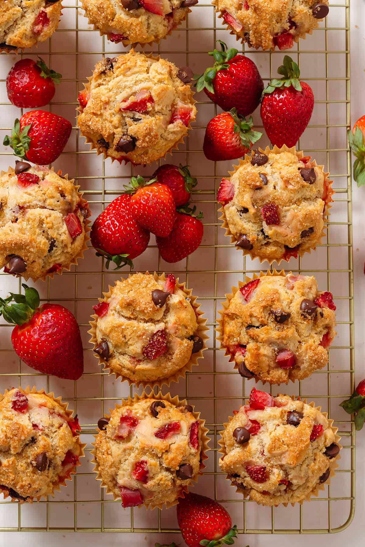 Strawberry chocolate muffins on a golden wire cooling rack with fresh strawberries around them.