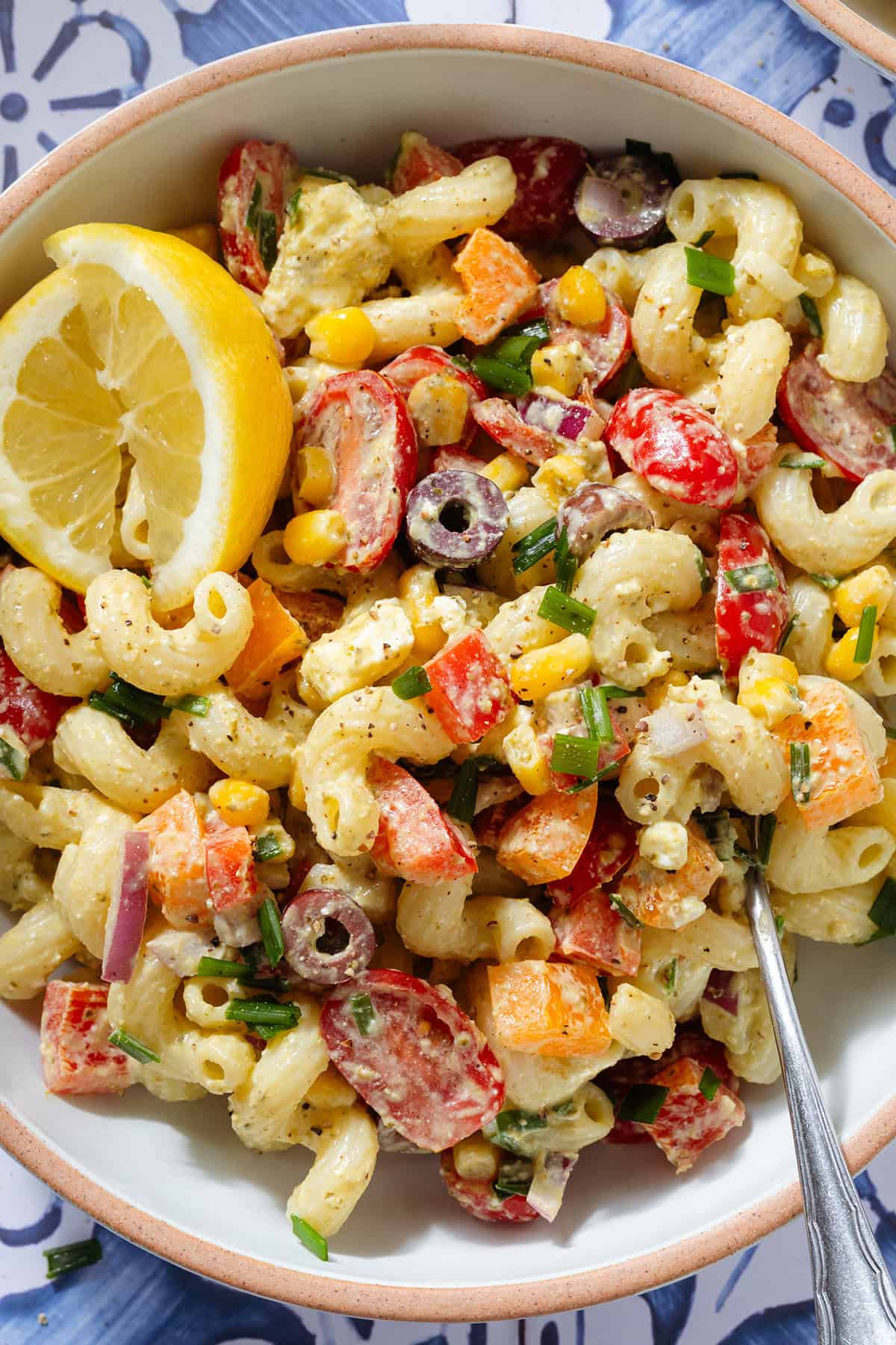 Colorful creamy pasta salad with two lemon wedges in a bowl with a fork on the right side.