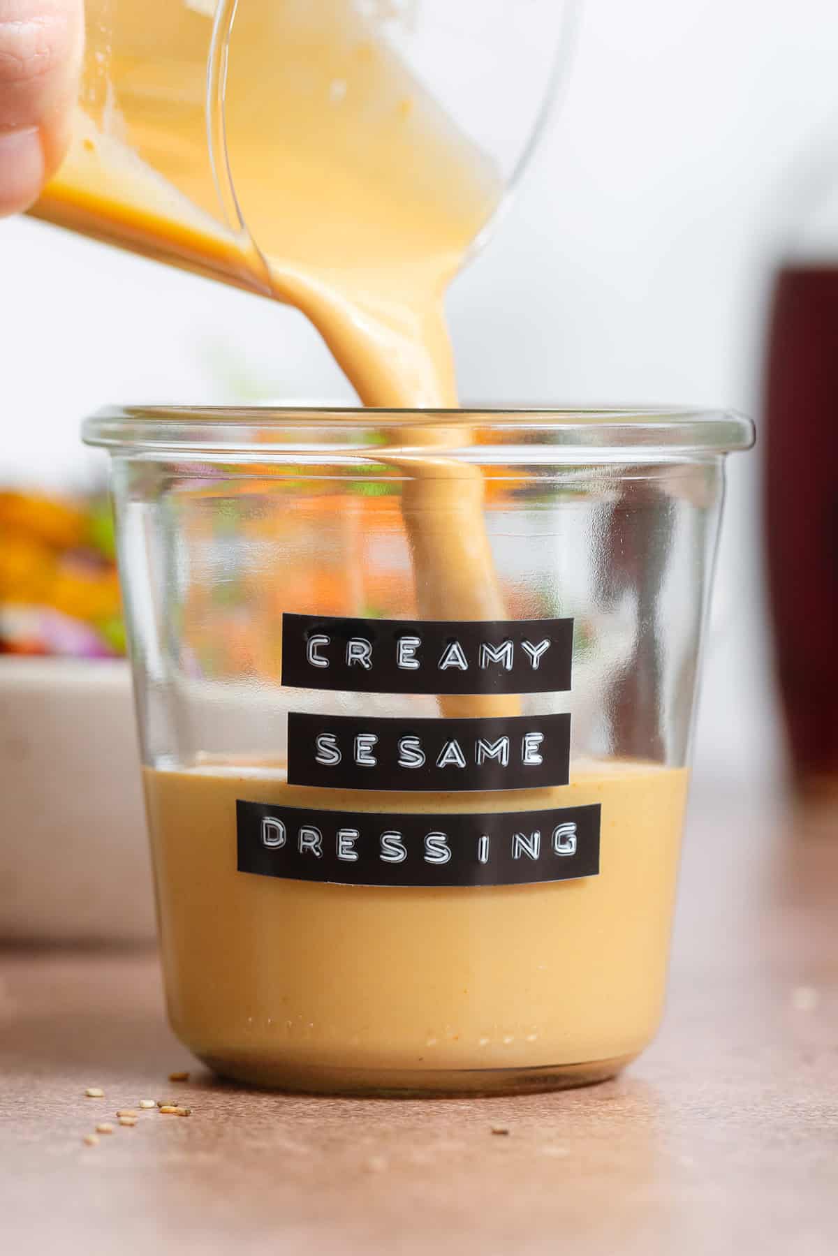 Golden creamy sesame dressing being poured into a short glass jar.