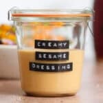 Golden creamy sesame dressing in a short glass jar.