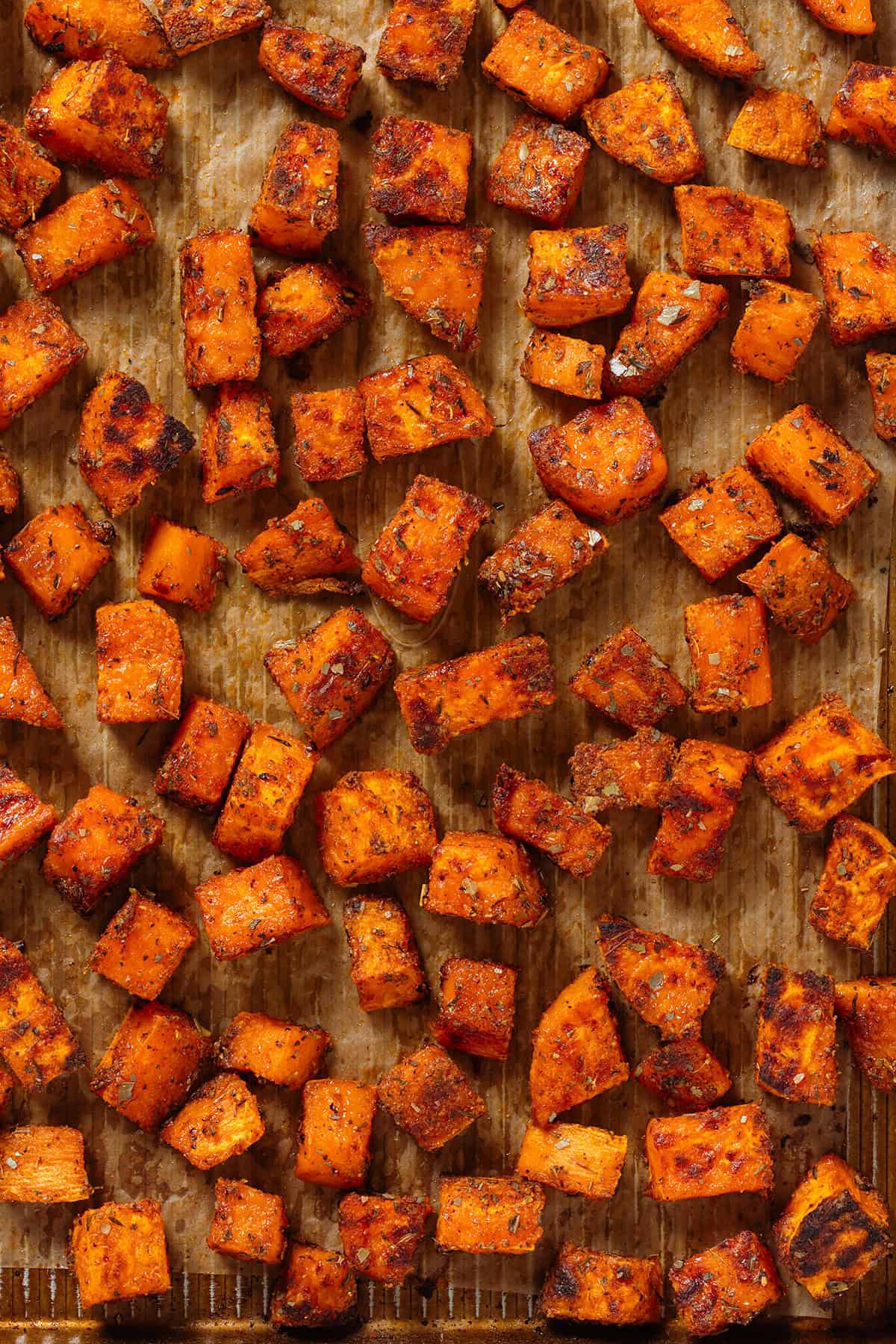 Extra crispy roasted sweet potatoes on a baking sheet lined with parchment paper.