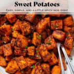 Crispy charred roasted diced sweet potatoes in a white bowl with a beige rim sprinkled with flaky sea salt and finely chopped fresh parsley and with two serving forks on the right.