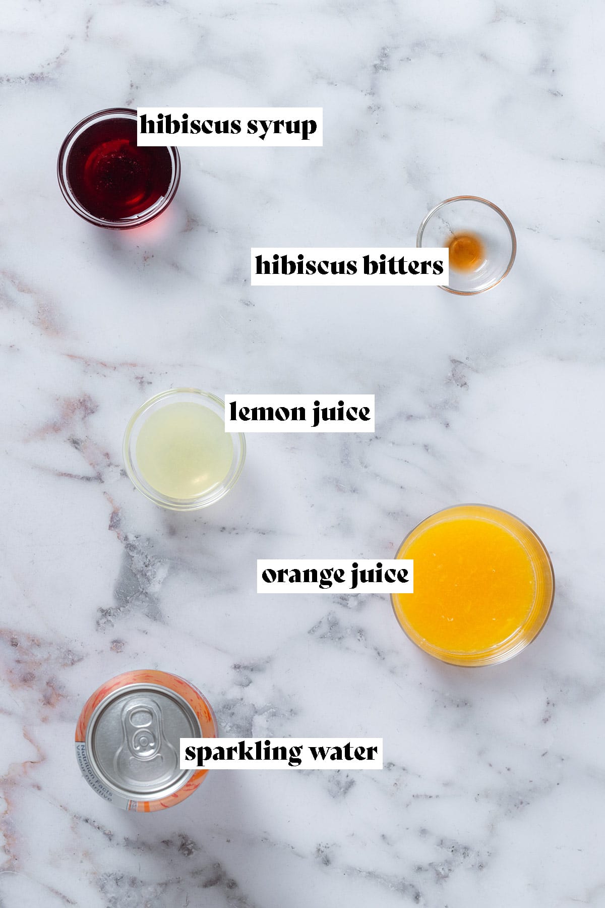 Sparkling water, hibiscus syrup, bitters, orange juice, and lemon juice laid out in small bowls with text overlay.