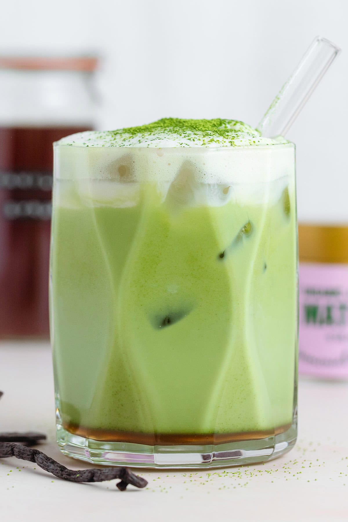 A matcha latte with cold foam on top dusted with matcha for garnish and a glass straw.